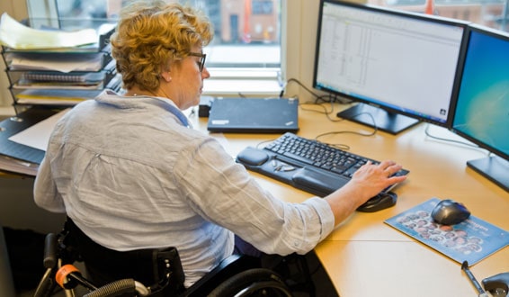 Kvinne i rulllestol ved kontorpult