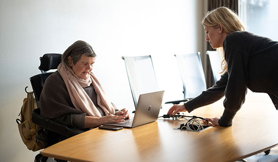 Kvinne i rullestol jobber på bærbar PC som funksjonsassistent kobler ledningen til