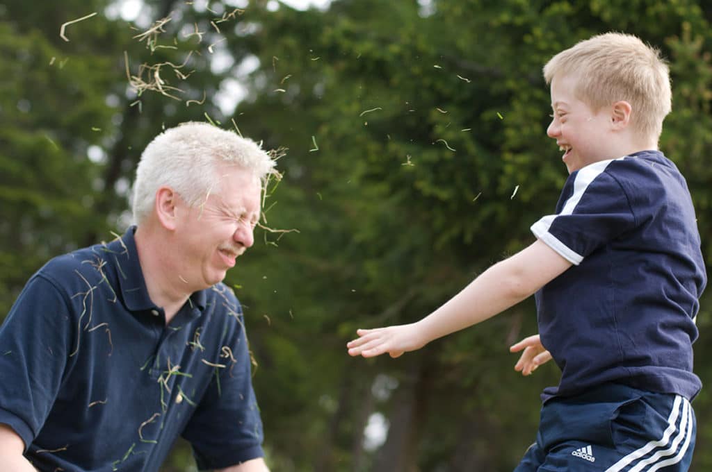 Funksjonshemmet gutt kaster gress i ansiktet på voksen mann og ler