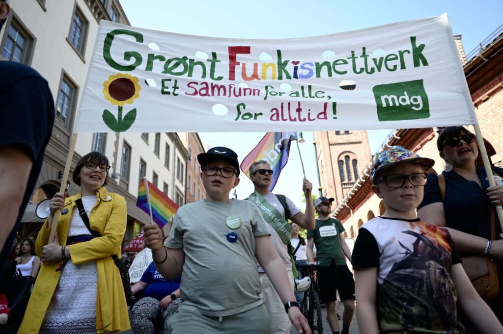 Grønt Funkisnettverk i Stolthetsparaden. Vi ser både voksne og barn holde en fargerik parole med teksten "Grønt Funkisnettverk – Et samfunn for alle, for alltid!" og MDG-logoen. Alle har på seg buttons og alle regnbuens farger. Til venstre i bildet er Suzanne Rødseth, som var med i den politiske debatten under Likestillingsbrølet.