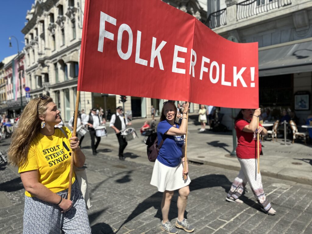 Tre festivaldeltakere i Stolthetsparaden holder parolen "Folk er folk!".