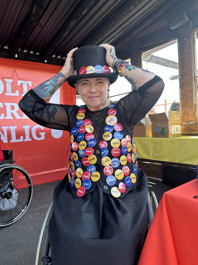 Ulobas Helle-.Viv Magnerud på Salt, iført en vest og en hatt fulle av festival-buttons. Hun holder på hatten sin og ser i kameraet. Hun har mange armbånd på og er tatovert på armene.