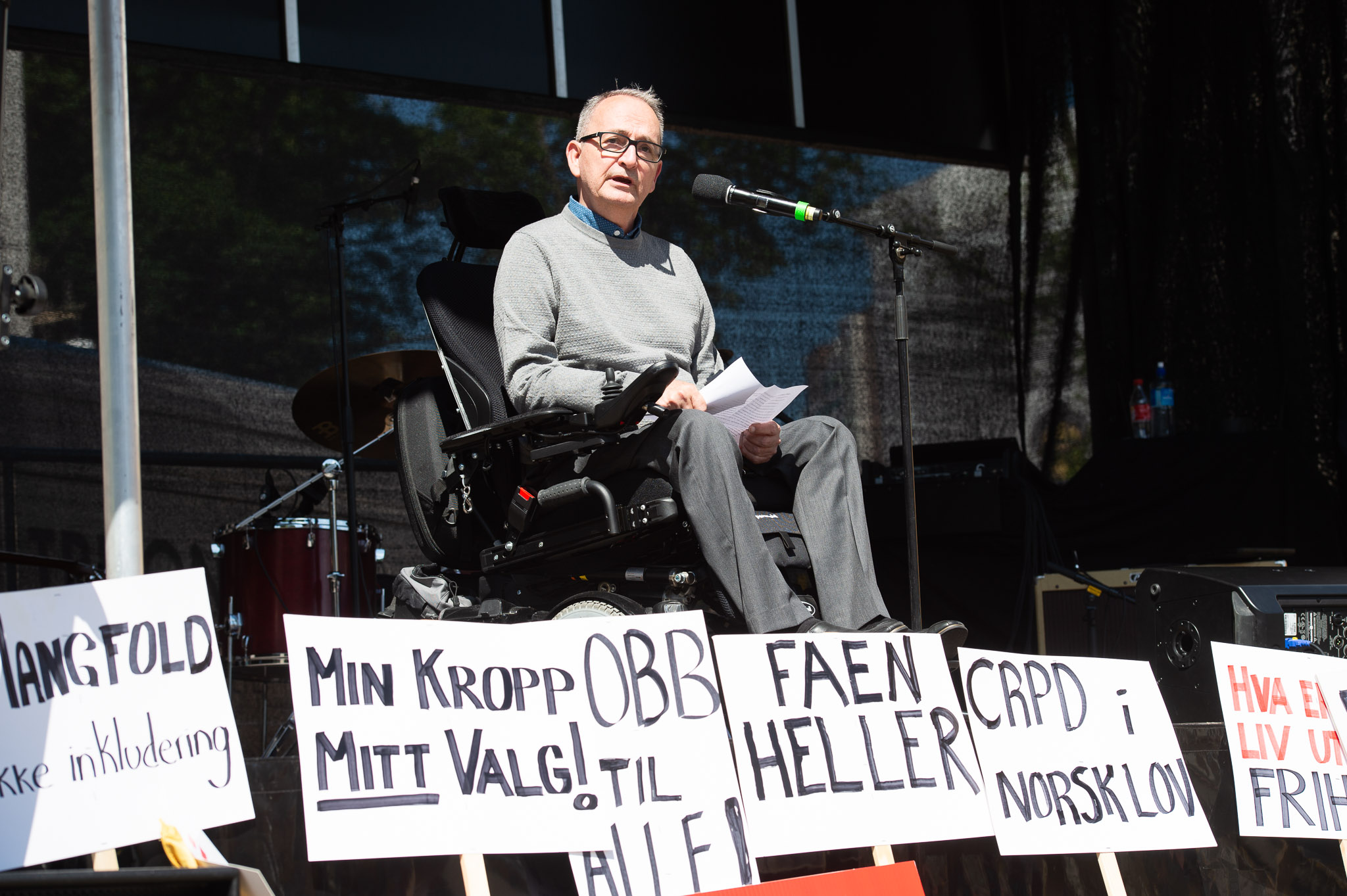 Lars Ødegård sitter på en scene blant paroler fra Stolthetsparaden. Han snakker inn i en mikrofon og har på seg blå skjorte og grå genser. 