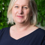 Ingeborg Rasmussen har grått, halvlangt hår, blå øyne og mørkeblå bluse. 