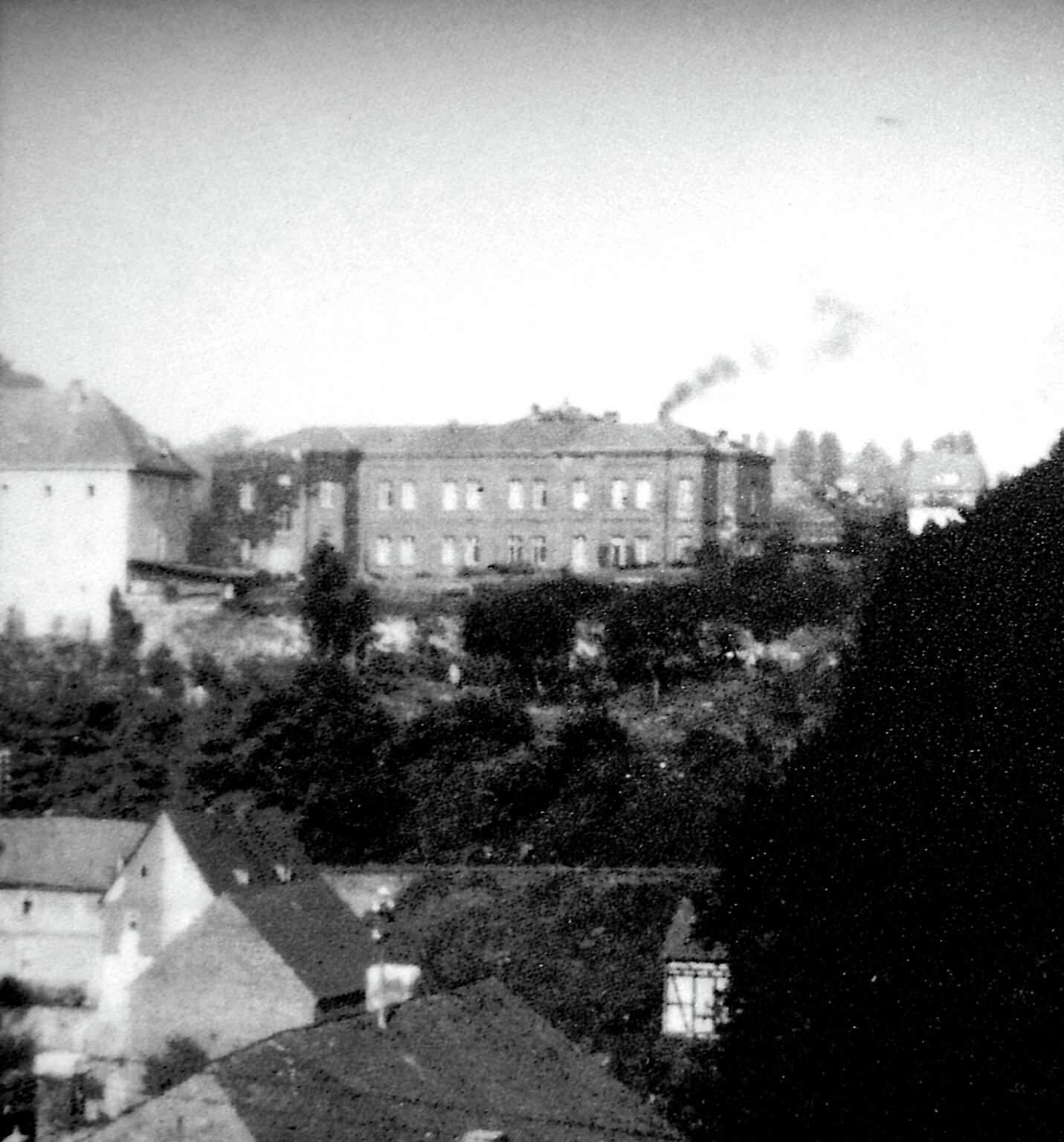 Dette biletet er teke i skjul i 1941. Bygget øvst i midten av fotografiet er NS Tötungsanstalt Hadamar, og røyken som stig opp frå pipa kjem frå krematoriet. Foto: Gedänkstatte Hadamar/Landeswohlfahrtsverband Hessen