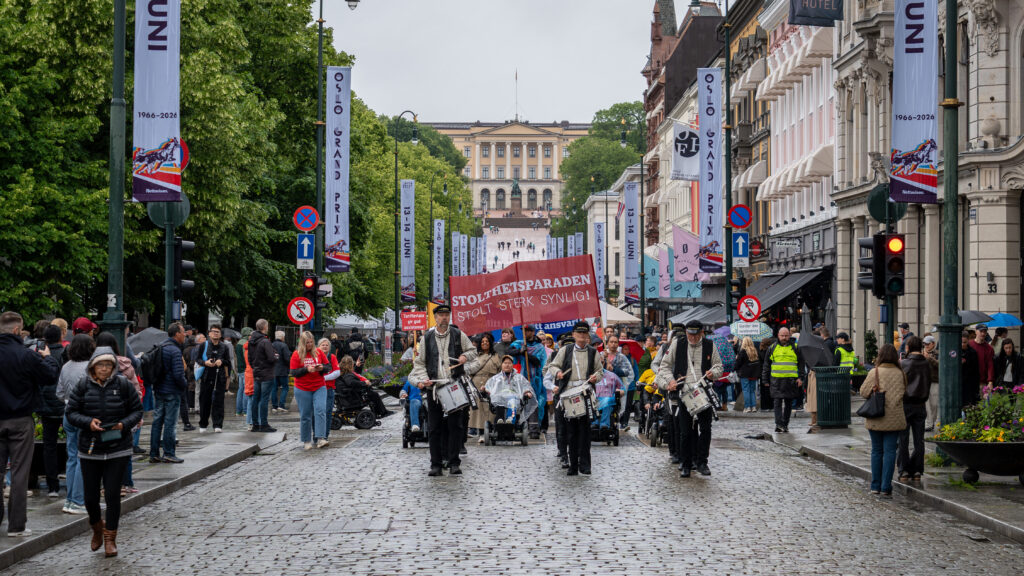 Stolthetsparaden på veg nedover Karl Johan, biletet er teke forfrå, med trommekorpset i front og Uloba-leiinga med hovudparoler rett bak. I bakgrunnen ser vi slottet.