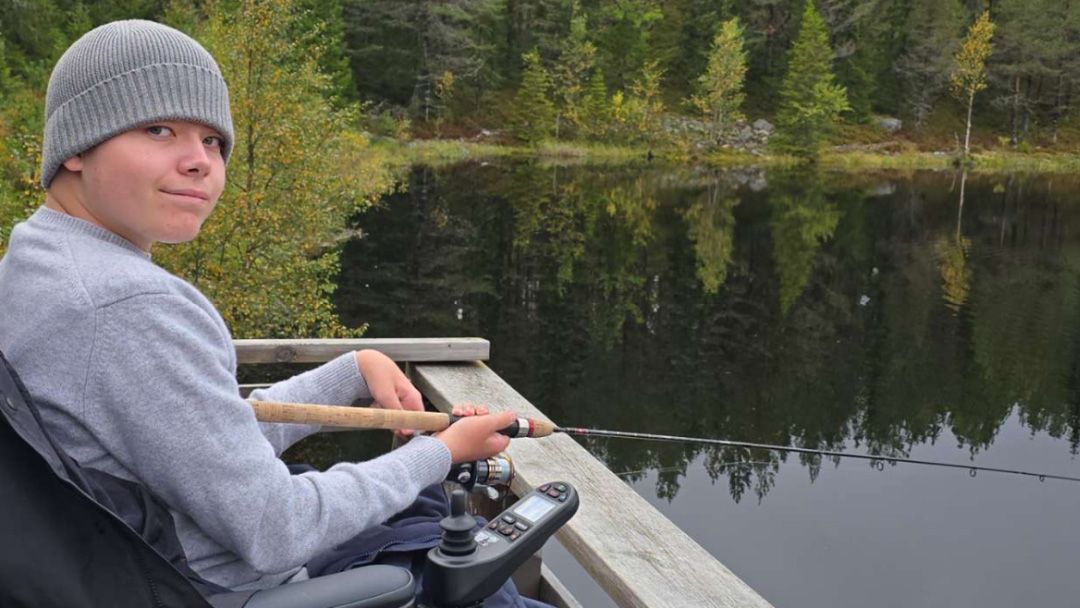 En ung gutt som fisker, han sitter i en elektrisk rullestol.