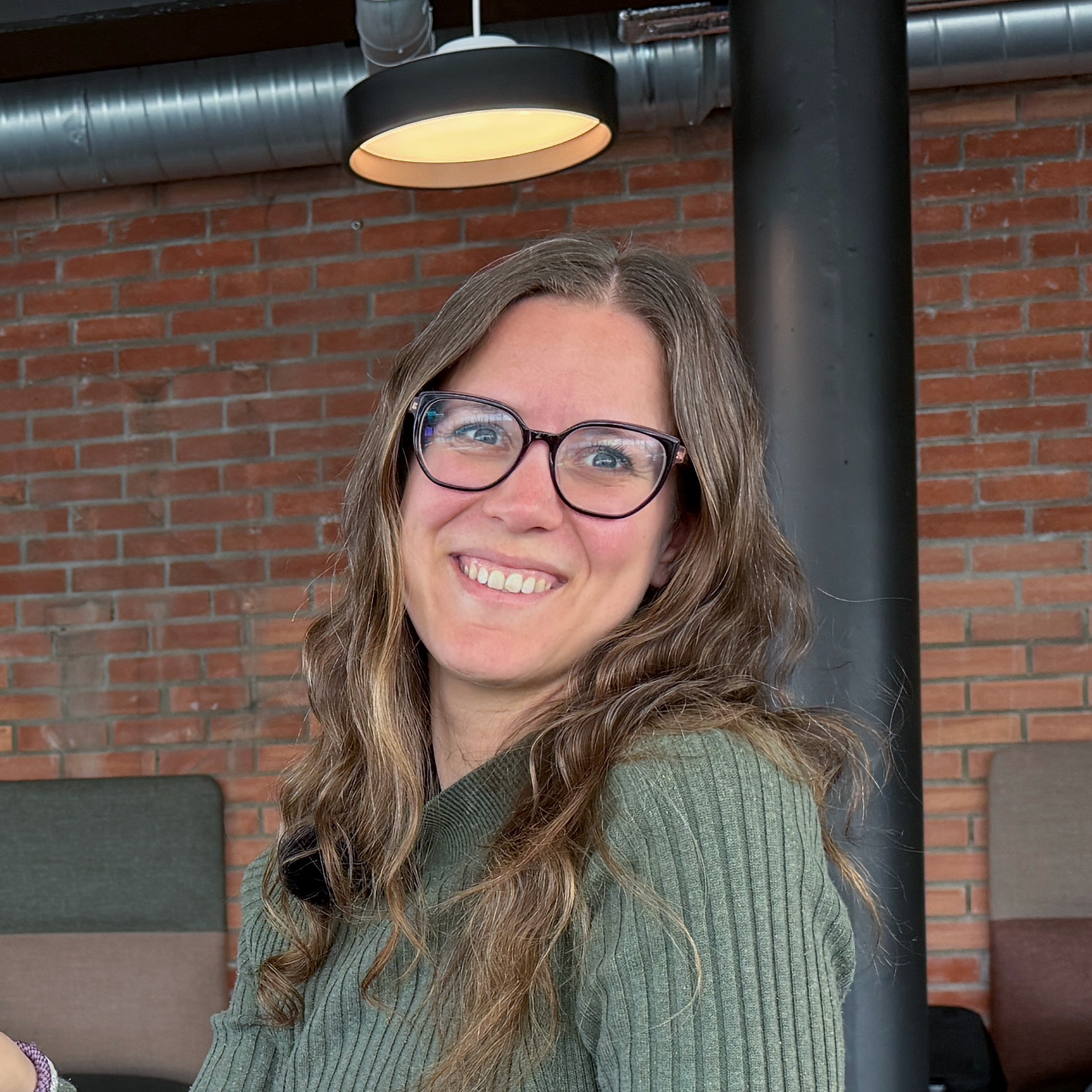 Bilde av Stine Sæther Jåthun som smiler til kameraet. Hun har langt bølgete brunblodt hår, blå øyne, briller og en mørkegrønn strikkegenser.